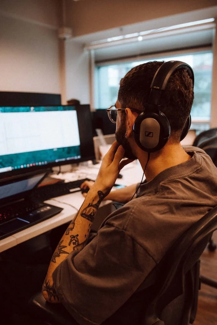 Home Young adult man focused on computer screen while wearing headphones in an office setting.