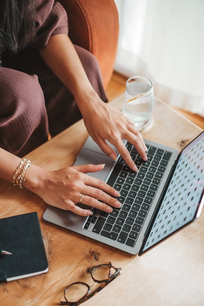 Close-up of a woman typing on a laptop with eyeglasses on the table, reflecting work and focus.